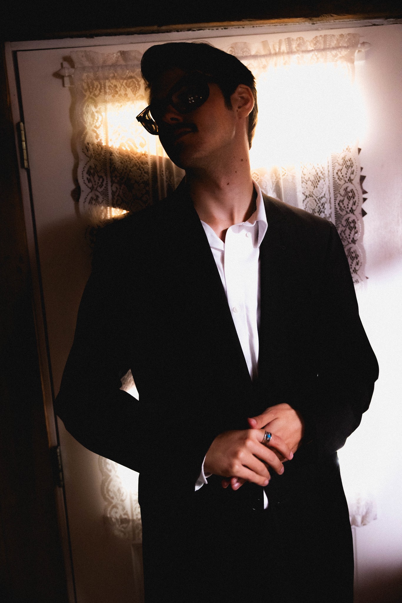 A suited figure in sunglasses, caught in the light of an open doorway.