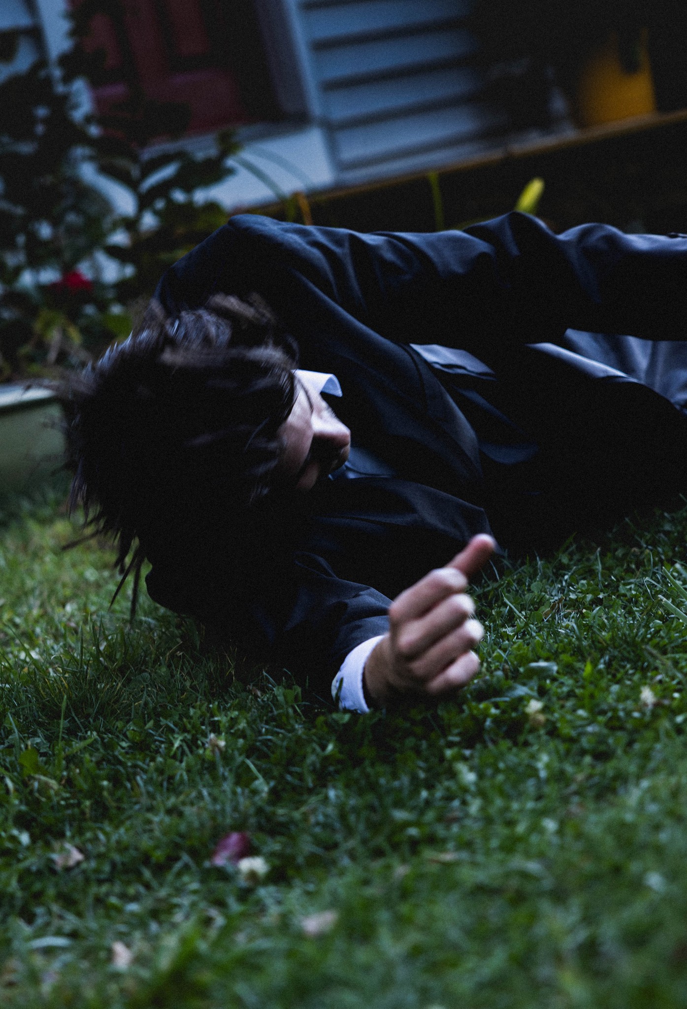 A reclining figure photographed close to the grass in cool light.