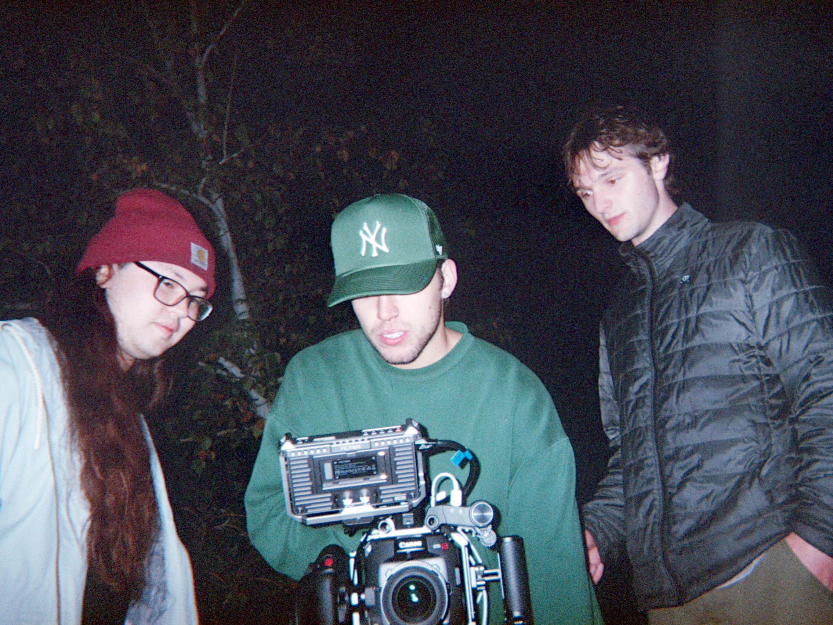 Three people gathered around a camera outdoors at night.