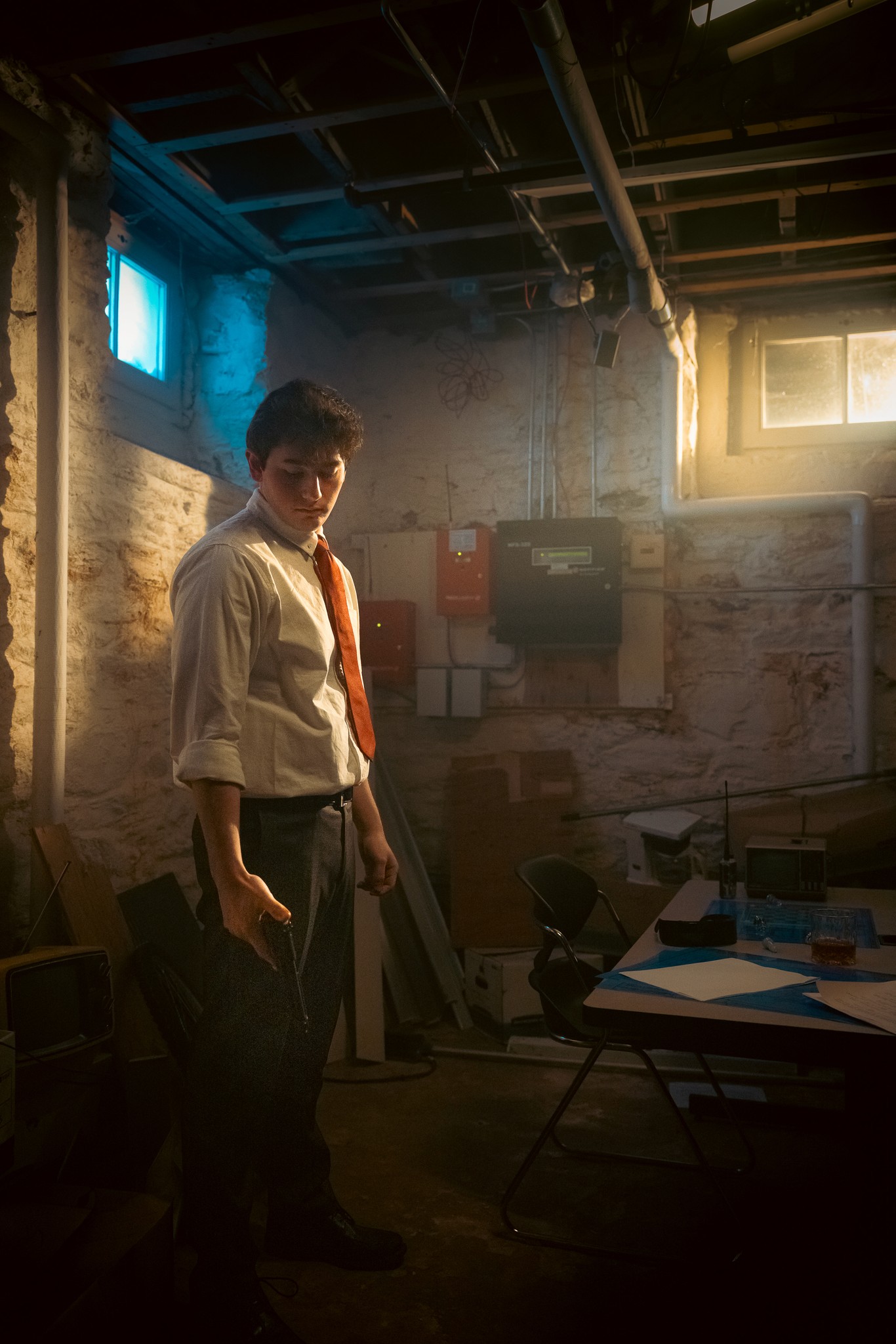 A figure in a workroom, surrounded by tools, shadow, and warm window light.