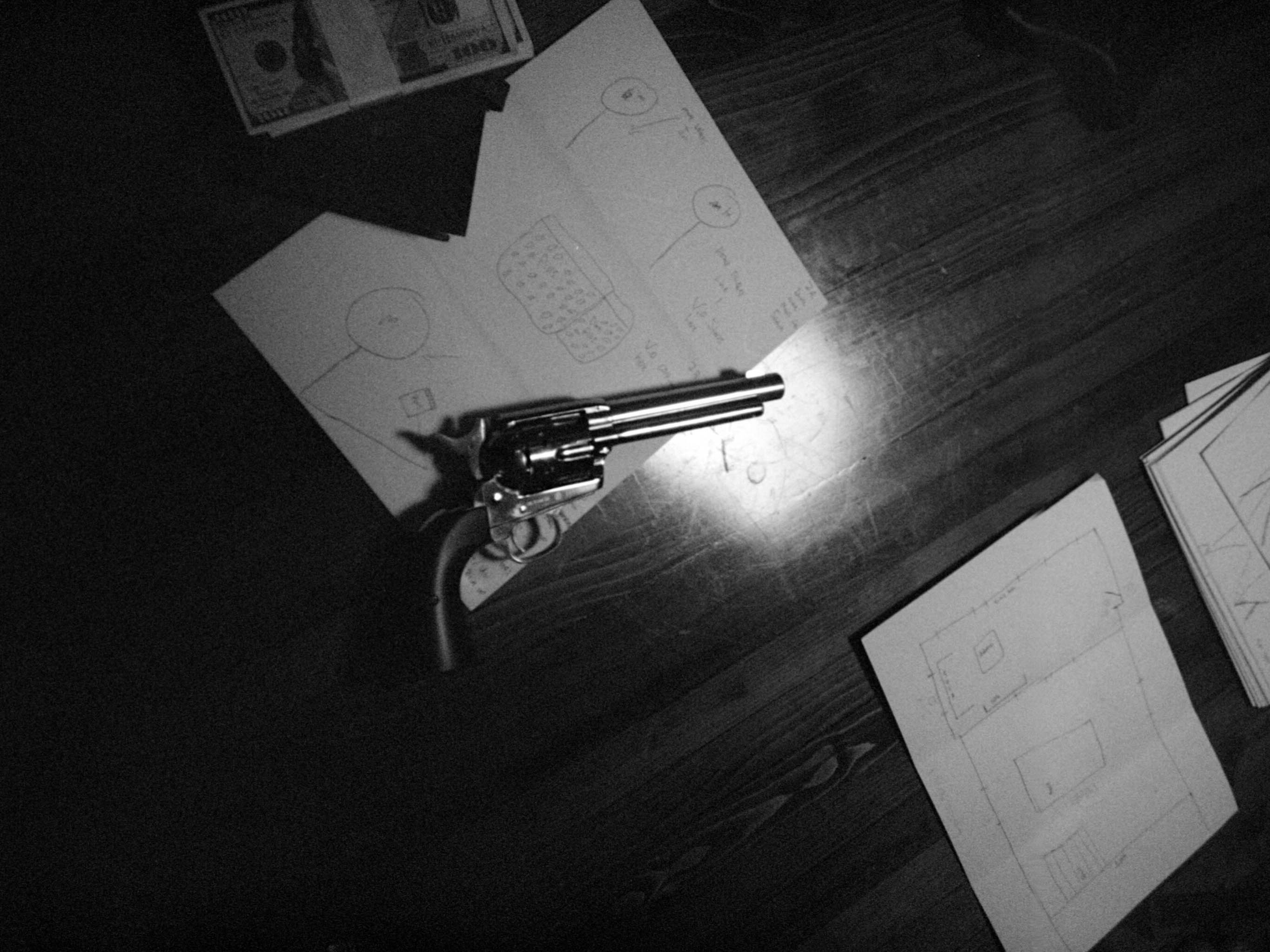 An overhead black-and-white study of a handgun-shaped object and papers on a wooden table.